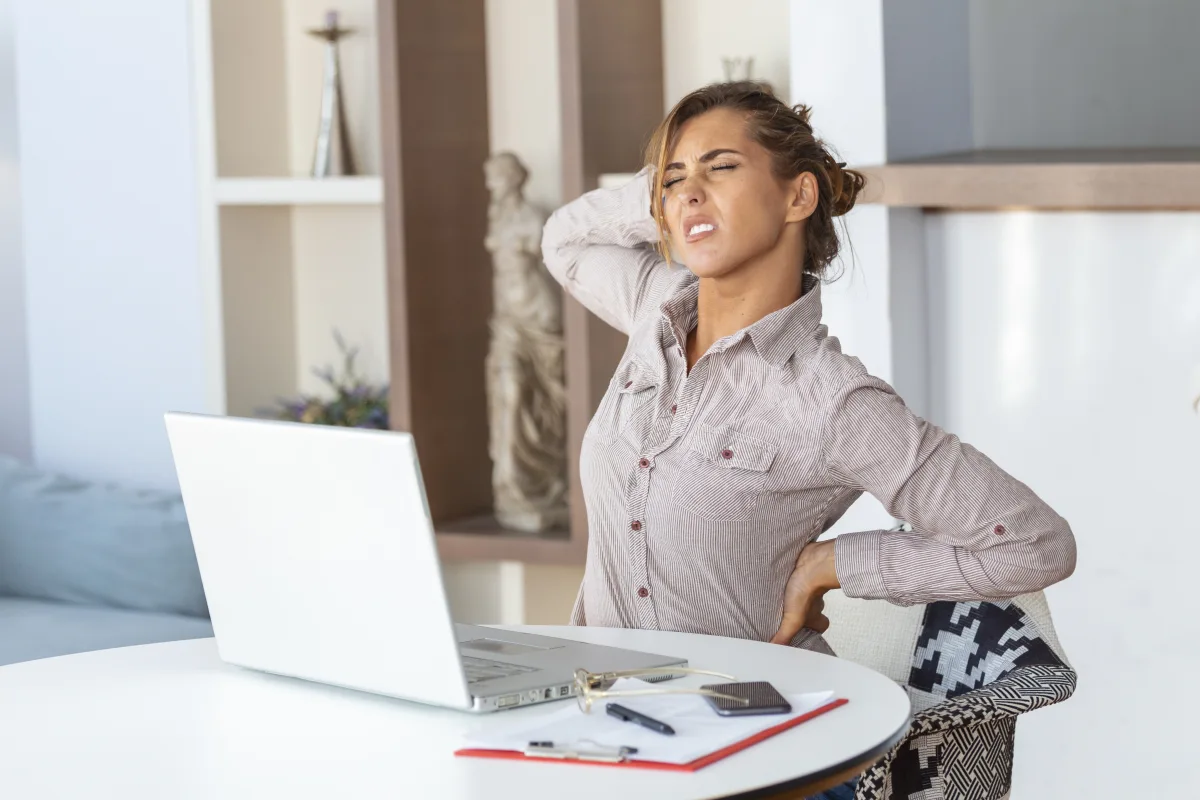 Woman experiencing back and neck pain while working at a desk