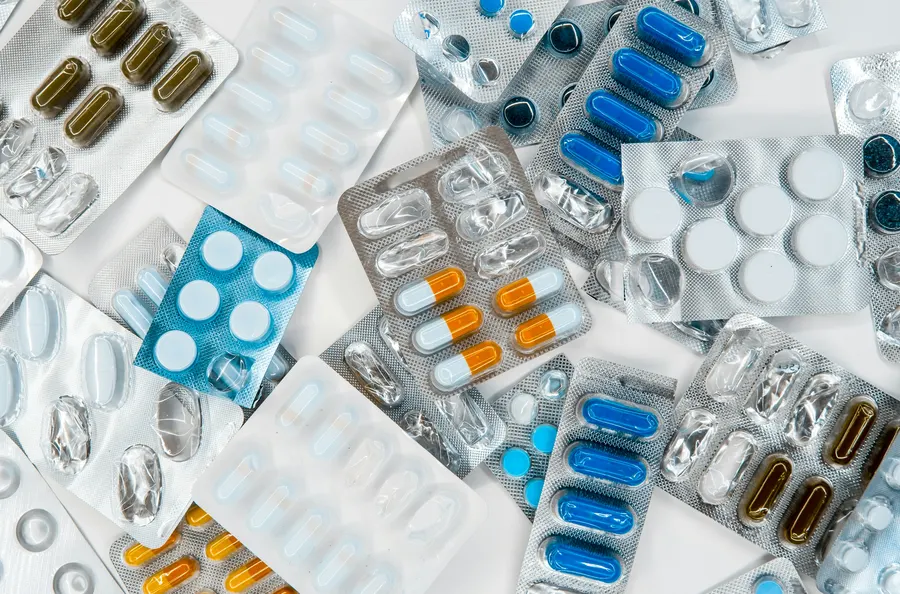 Multiple blister packs of pharmaceutical pills and capsules of different colors spread across a white surface