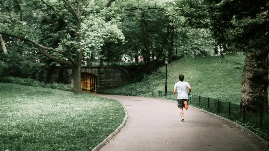 Man running along a green park path surrounded by trees