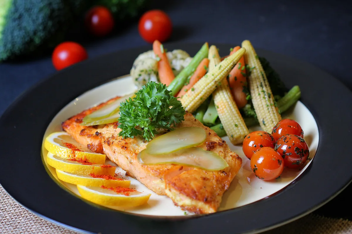 Grilled salmon with colorful vegetables on a dark plate