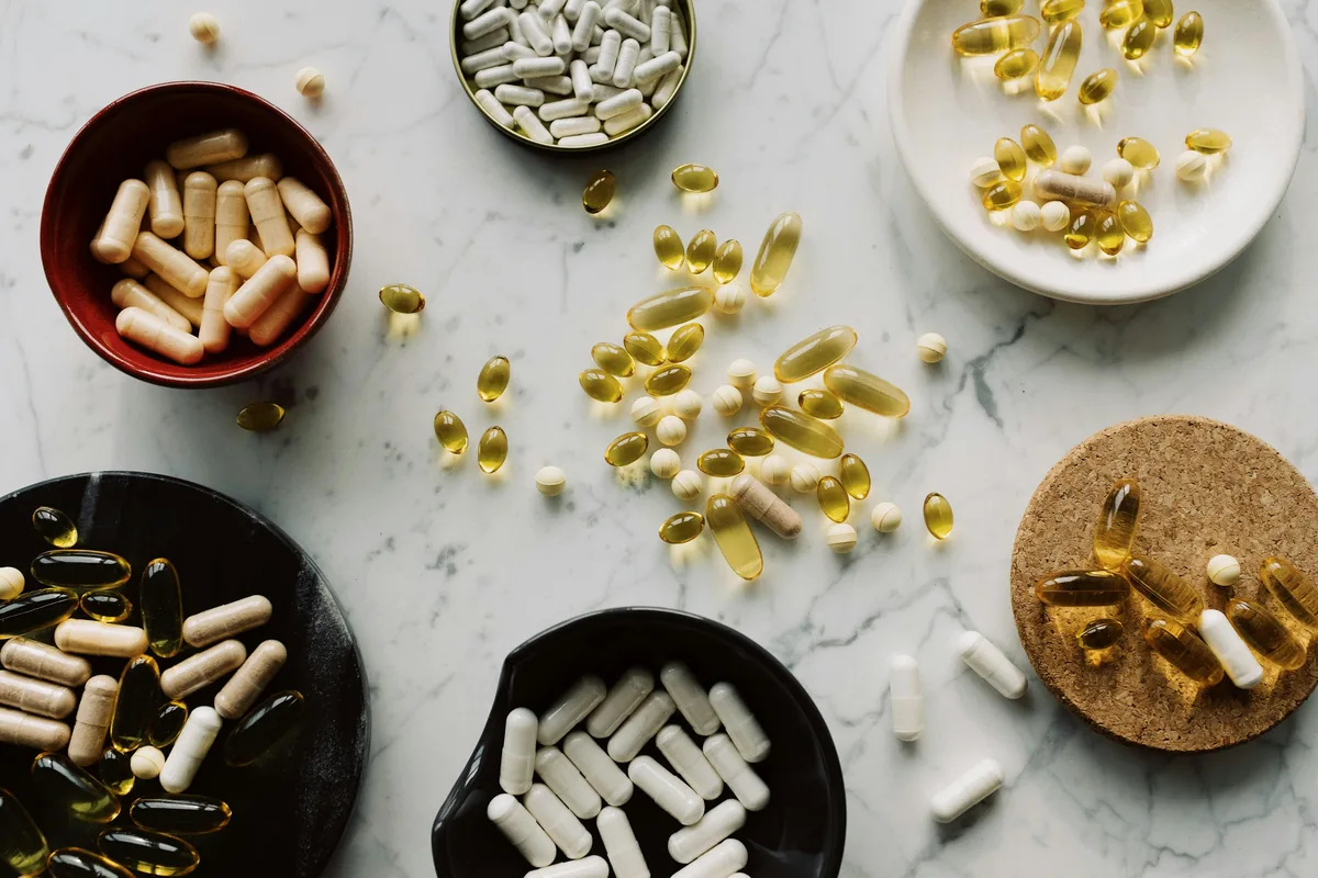 Various supplement capsules and softgels arranged in bowls on marble surface
