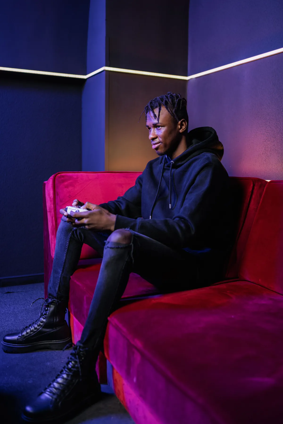 Teenage boy sitting alone holding a game controller in a dimly lit room