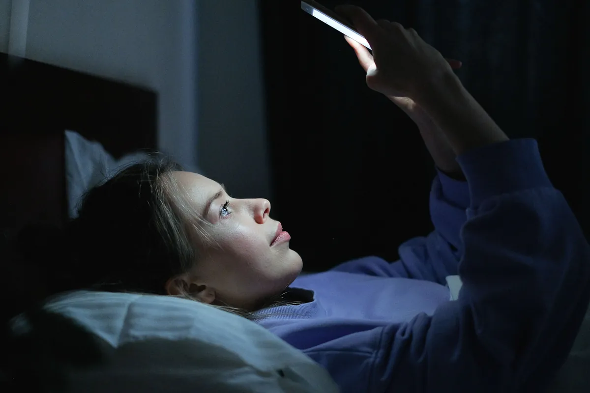 Teenager looking at phone screen in dark room before sleep, blue light illuminating face