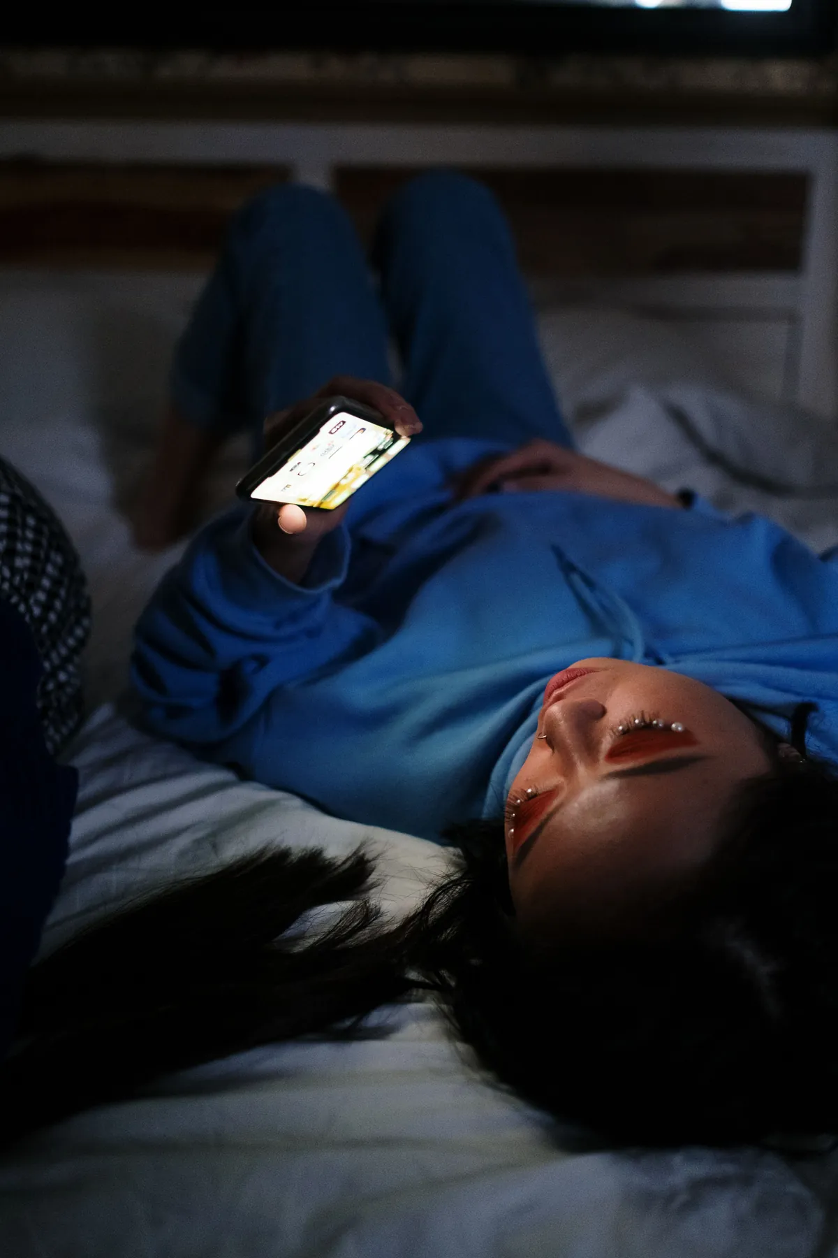 Glowing smartphone screen on a nightstand next to a sleeping teenager, representing sleep disruption from social media