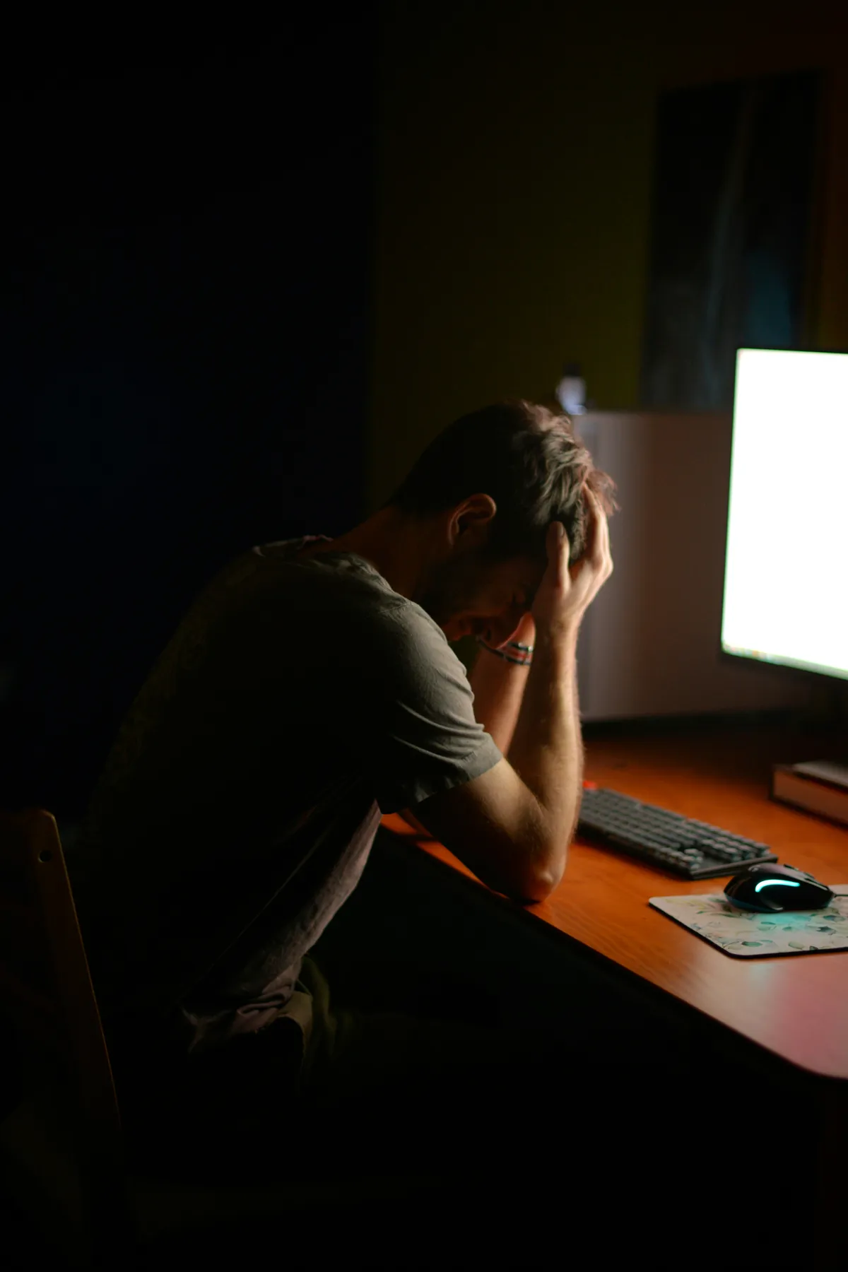 Man sitting at desk with head in hands in a dark room, representing chronic stress and burnout