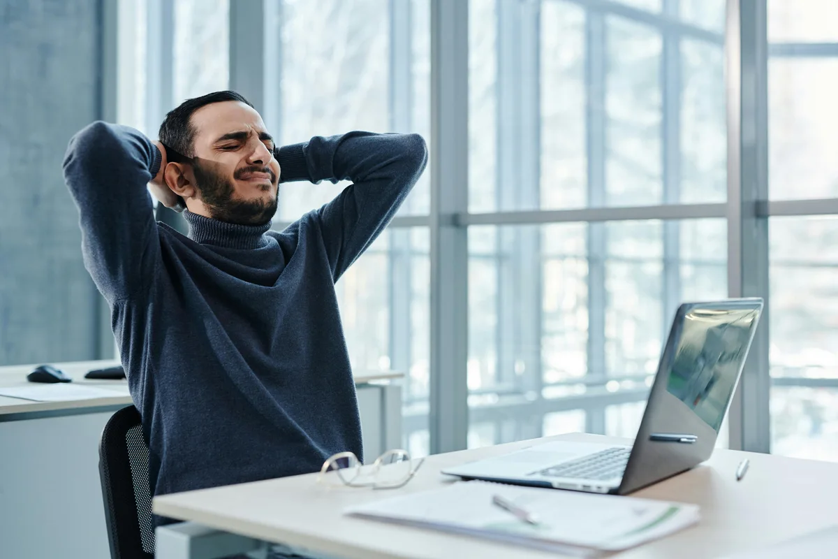 Man at a desk stretching his neck and upper back with visible tension and discomfort