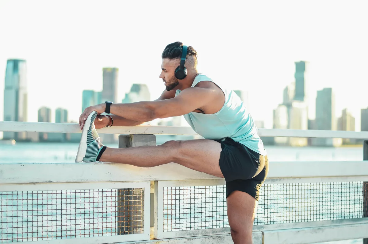 Male athlete stretching his leg dynamically against a railing with a city skyline backdrop
