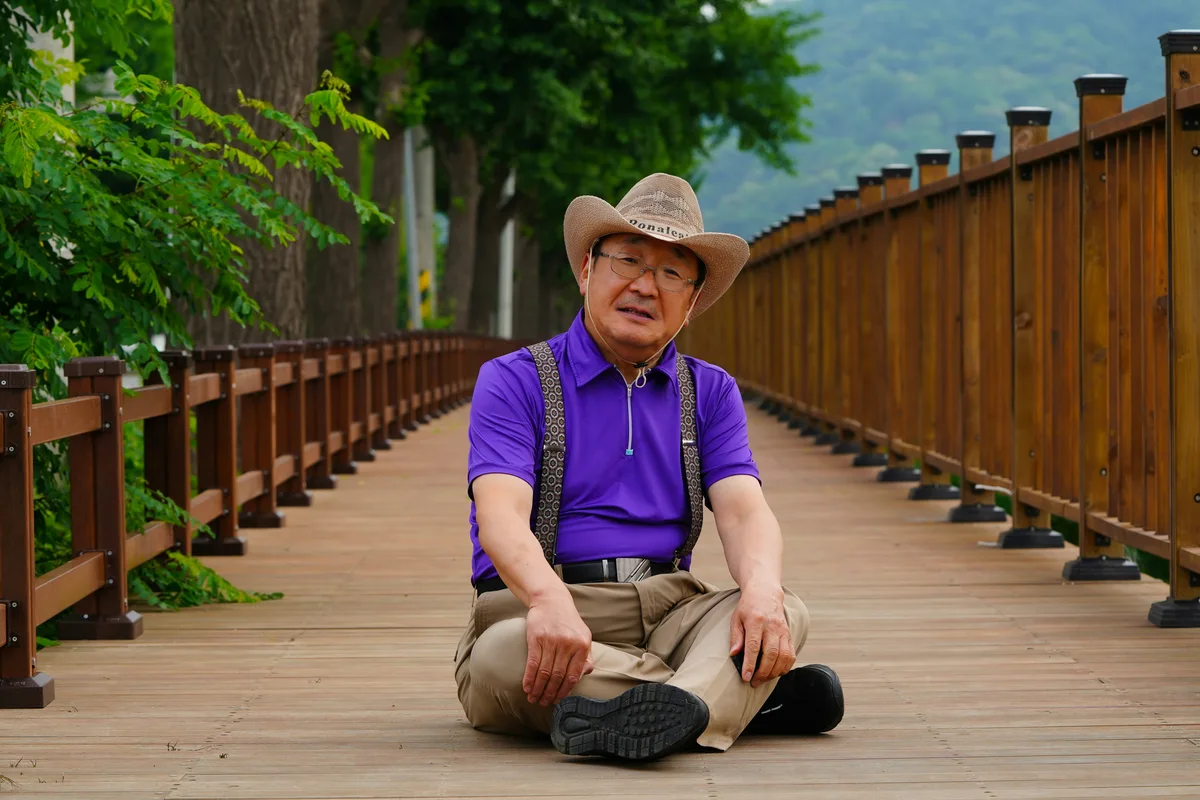 Older man sitting cross-legged on the ground outdoors, demonstrating floor-level mobility
